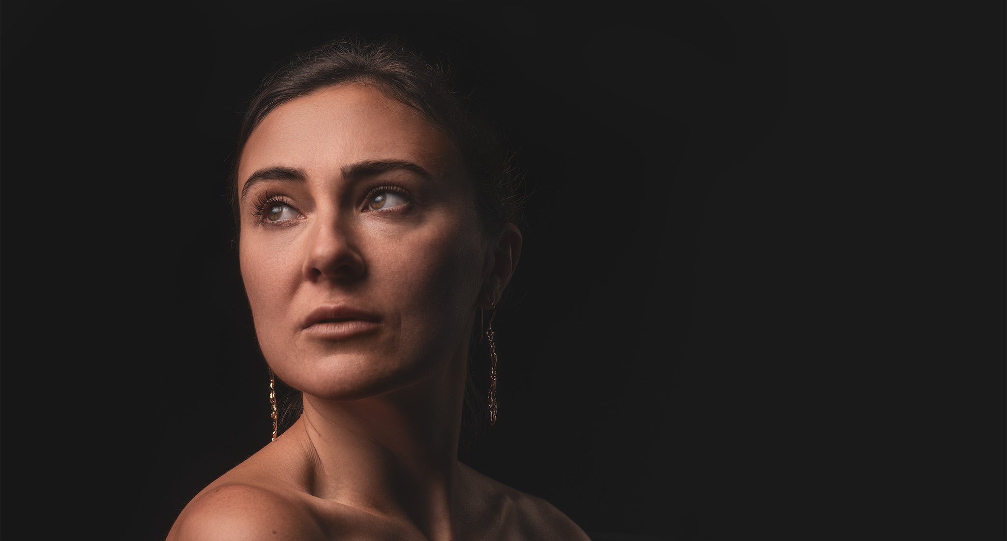 Artisan-crafted gold earrings by 'What If You Stayed' jewelry artist displayed on a model against a dark background.