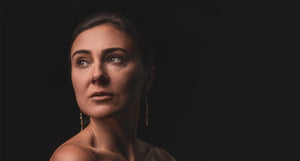 Artisan-crafted gold earrings by 'What If You Stayed' jewelry artist displayed on a model against a dark background.